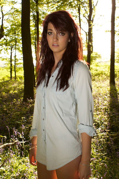 A girl in a forest setting looks at the camera while the fill-in flash illuminates her face