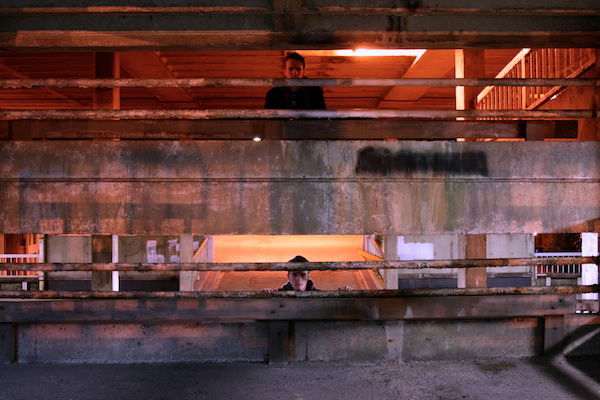 Two men on two floors of a parking lot looking through the railing