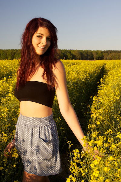 A woman poses in a field of yellow flowers. 