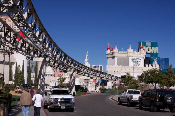 A photograph of an outdoor scene, featuring a skywalk structure with signs, people walking, and cars at the bottom. 