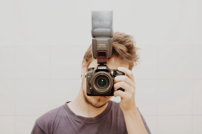 A photographer holding up a camera and flash to his face to take a picture