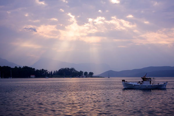 A sunset over a lake or body of water, with clouds and the light beaming through them. 