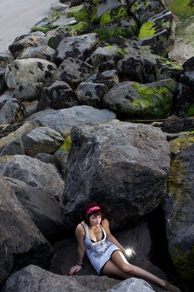 a girl sitting between huge rocks at the bottom of the frame