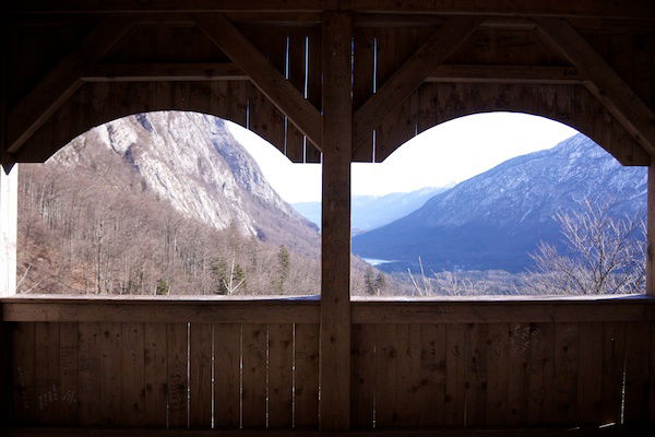 A wooden barn or stable with large openings revealing the mountain scenery beyond. 