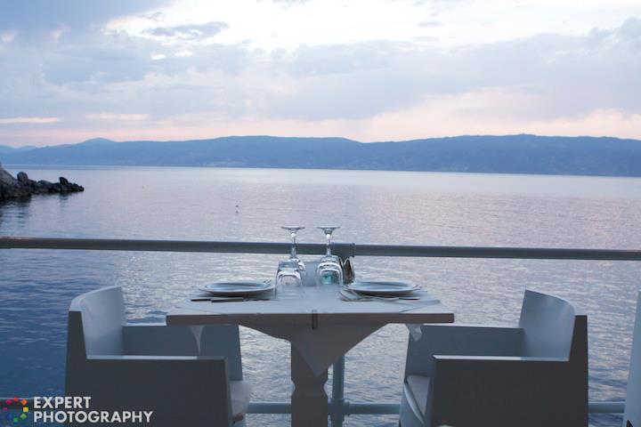 A table set by the sea at evening time with an 'Expert Photography' watermark on the bottom left corner