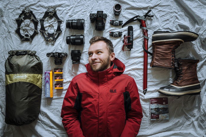 Man laying next to camera equipment laid out on a bed