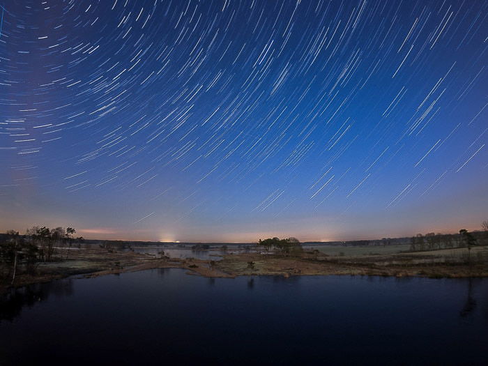 Nocurnal landscape over water, creative motion blur star trails above 