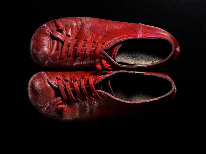 A pair of red camper shoes on a black background