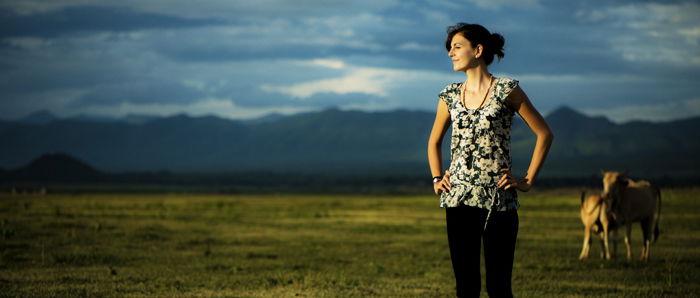 Photo of a woman outdoors with cows and mountains in the background