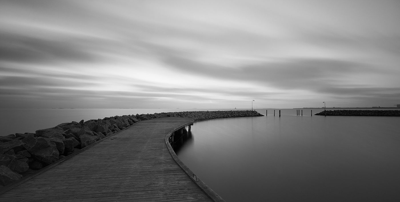 Monochrome image of water's edge with cloudy sky and still water