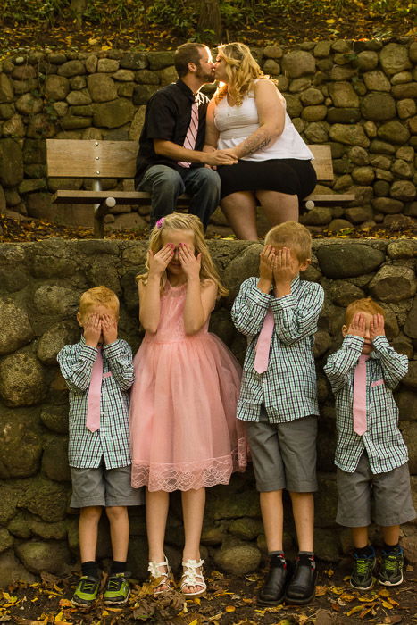 A couple kissing on a bench, 4 kids below 