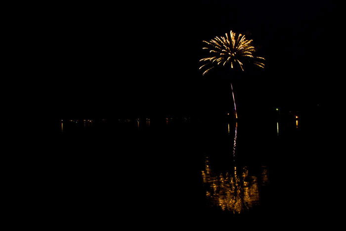 Amazing fireworks photography of yellow burst over water in the distance