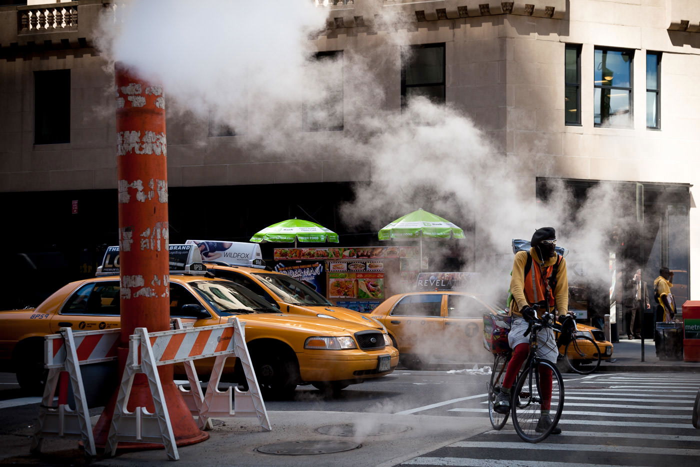 Street photography: NYC bike messenger in street with steampipe