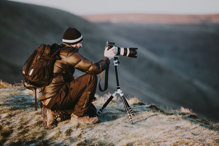 Man on mountain top mounting a camera on a tripod