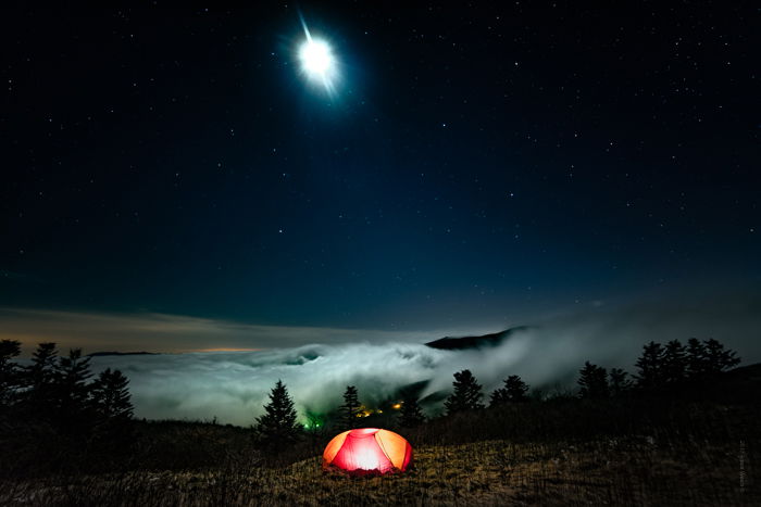 Dramatic Weather: Heavy fog rolling in on the horizon at night, with illuminated tent in foreground