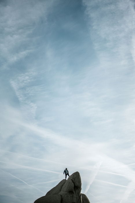 A person standing on a rock, with a blue sky behind them 