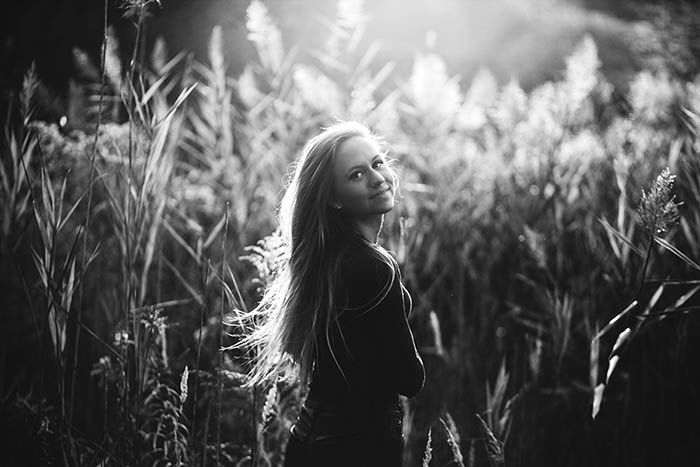 Monochrome portrait of a young woman in a field, looking over her shoulder at the camera.