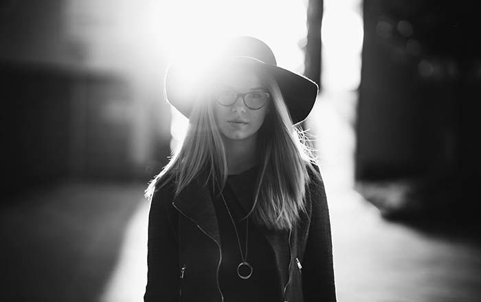 Greyscale portrait of a young woman wearing a hat and glasses. 