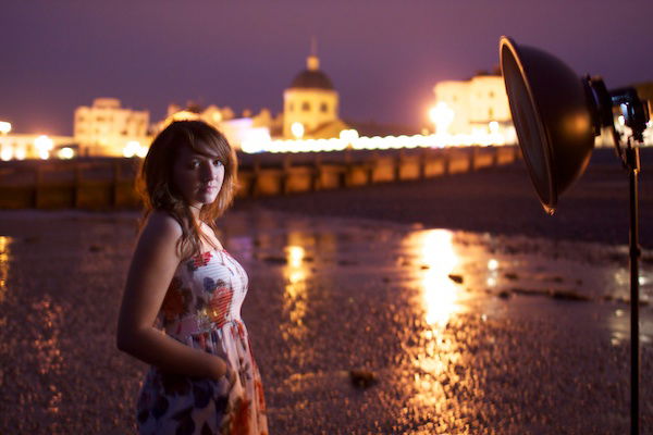 Portrait photography of a girl standing on a beach, harbour in background. Twilight photography.