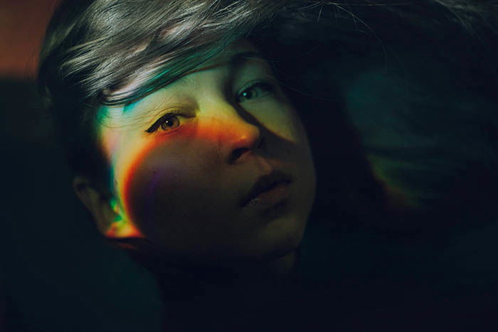 Mysterious self-portrait photography showing rainbow effect on a girls face created with a CD