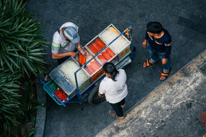 An overhead shot of a person selling food in a cart to two customers as an example of street photography