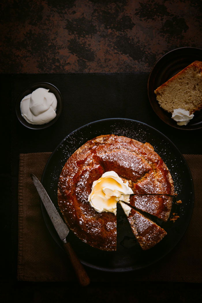 A freshly baked cake with cream and butter on the side, placed on a table with a knife. 