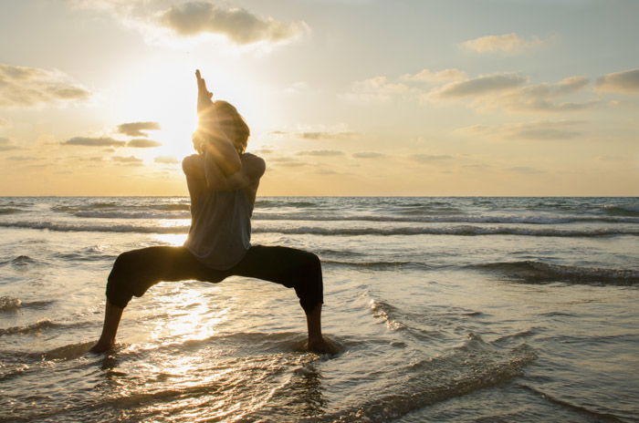 A silhouette of a woman doing yoga at sunset at a beach location