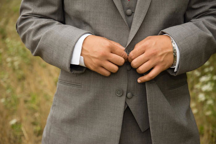 A Wedding portrait close up of a groomsman buttoning his jacket 