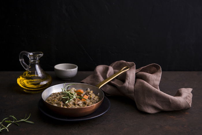 Still life food photography image of lentil soup in a copper pot on table