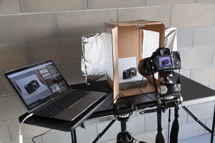 A photoshoot setup containing a laptop, diy light box, dslr camera on tripod