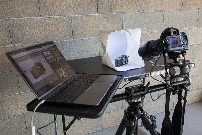 A diy photoshoot setup containing a laptop, diy light box, dslr camera on tripod