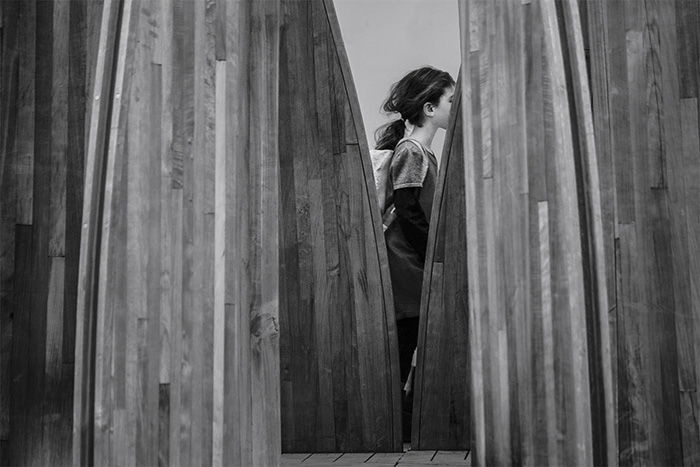 Black and white photo of a little girl framed by the artwork 'Tree Houses for Swamp Dwellers', Julia Morison, 2013. Christchurch, New Zealand. Architecture Photography.