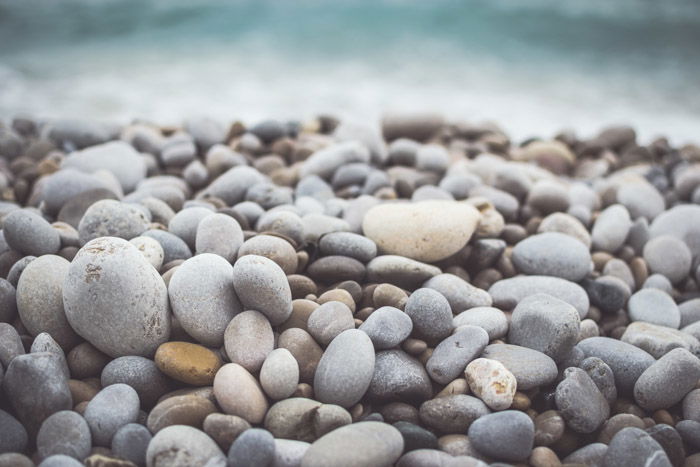 A close up photo of colorful rocks with bokeh effect of the waves in the background