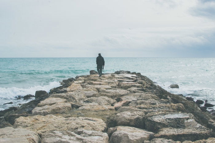 A lonely figure walking on a pier surrounded by the sea and the sky