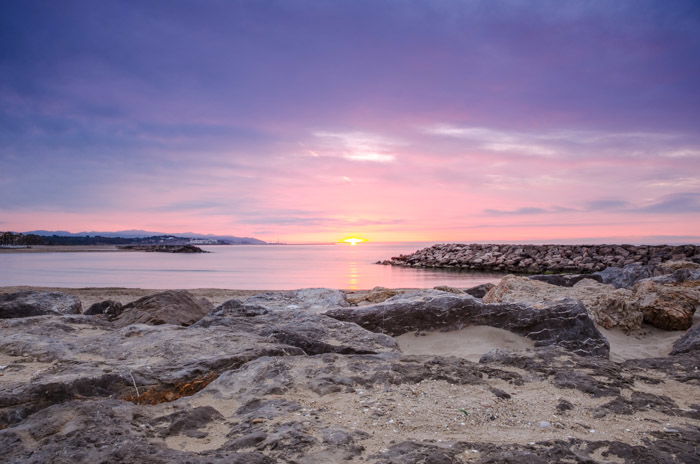 A beautiful beach landscape at sunset, with rocks in the foreground and a pink sky in the background