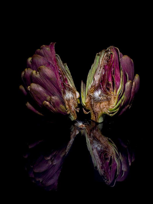 An artichoke cut in half in front of a black background with its reflection