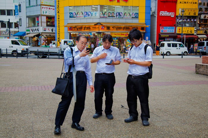 three men looking at their phones on the street