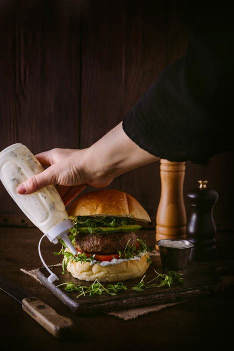 adding sauce to a burger using a squeeze bottle