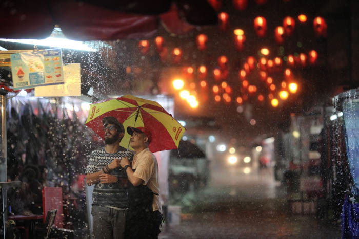 Two men in a rainy outdoor market at night, lit by colorful lanterns