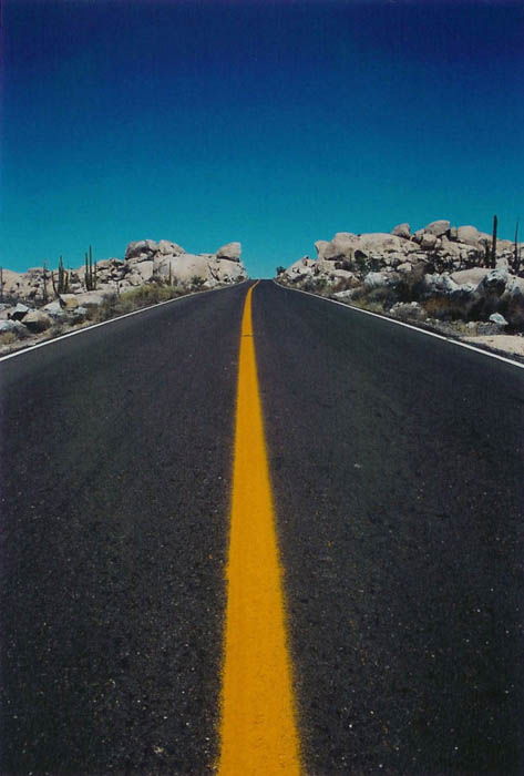 road photo of a highway leading into the horizon, blue sky and yellow striped road