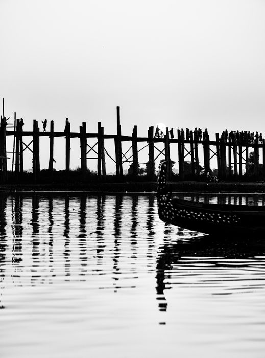 Black and white travel photo of the U-Bein bridge in Myanmar, the bridge and a boat nicely reflected in the water