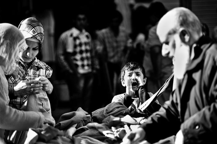 Black and white travel photo of a market in Istanbul, a young boys shouts towards the camera while adults look through fabrics