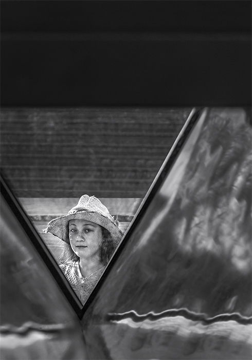 Black and white photo of a girl in white hat framed by architectural detail. Creative street photography