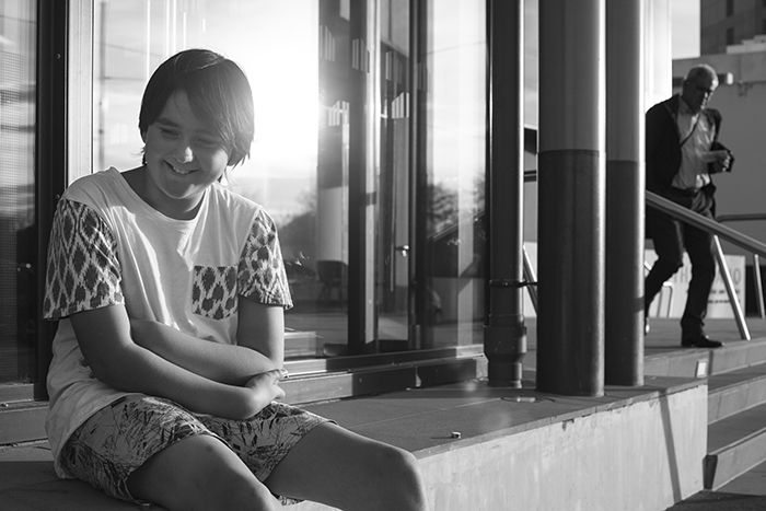 Black and white photo of a young boy sitting on a step. Creative street photography