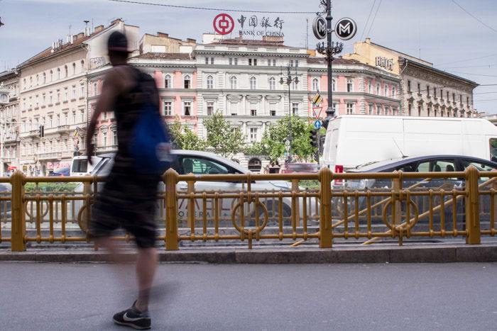 A street scene in Budapest with a blurred figure walking past cars and buildings.