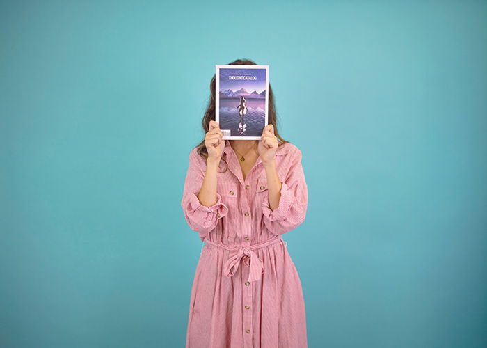 A woman in pink using a magazine to create a faceless portrait to advertise her business