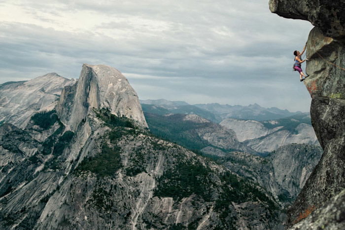 Adventure photography of a woman rock climbing in a vast mountainous landscape by Andy Bardon.