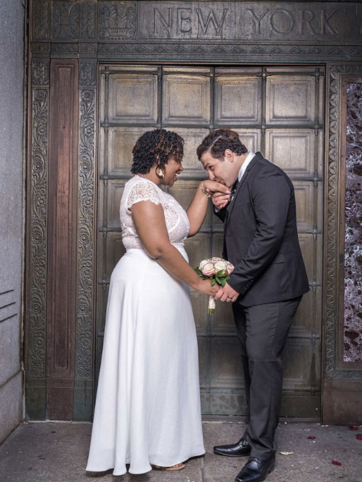  Wedding photography of newlywed couple holding hands outside a doorway by Wayne Lawrence. 