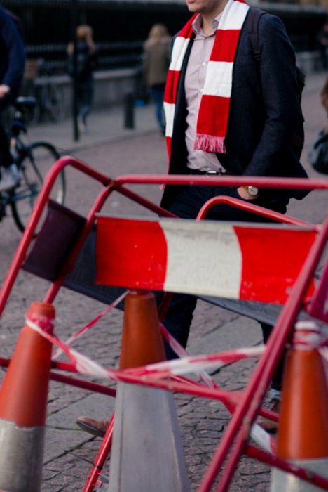 Street photography of a man wearing a scarf that resembles the environment in the road work barriers and tape. 