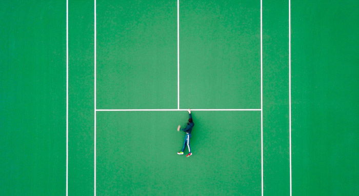 Overhead photo of a man on a tennis court but looks as though he is holding onto a ledge for dear life